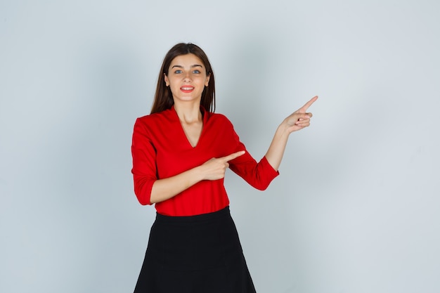 Junge Dame zeigt nach rechts mit Zeigefingern in roter Bluse