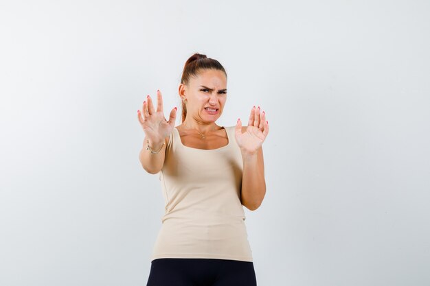 Junge Dame zeigt Stoppgeste im Unterhemd und sieht angewidert aus. Vorderansicht.