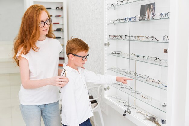 Junge, der auf Brillen bei der Stellung mit weiblichem Optiker im optica zeigt