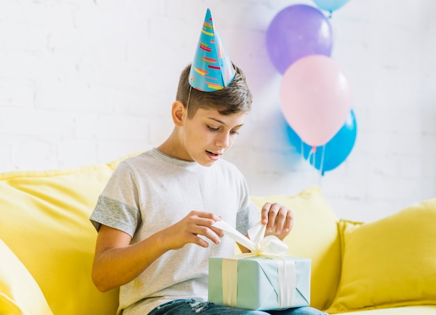 Junge, der auf dem Sofa auspackt Geburtstagsgeschenk sitzt