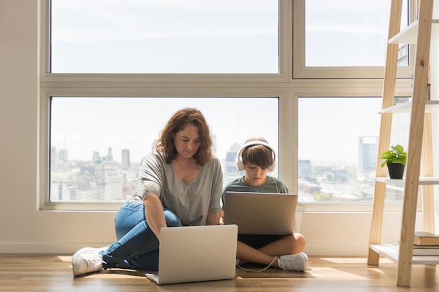 Junge, der auf Laptop neben Mutter spielt