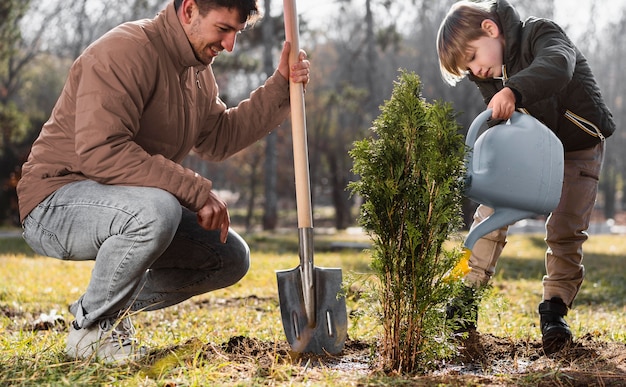 Kostenloses Foto junge, der einen baum im freien pflanzt und gießkanne verwendet