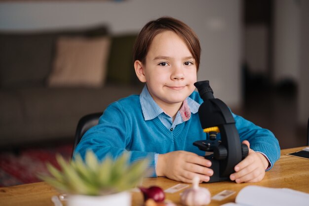 Junge der ersten Klasse, der zu Hause unter Verwendung des Mikroskops studiert