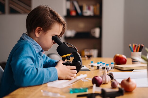 Junge der ersten Klasse, der zu Hause unter Verwendung des Mikroskops studiert