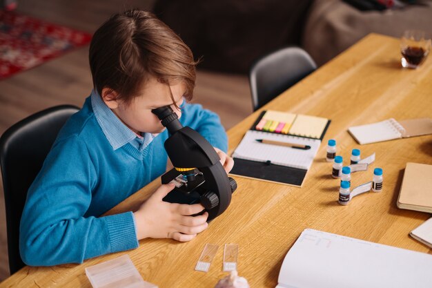 Junge der ersten Klasse, der zu Hause unter Verwendung des Mikroskops studiert
