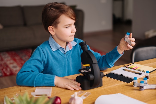 Junge der ersten Klasse, der zu Hause unter Verwendung des Mikroskops studiert