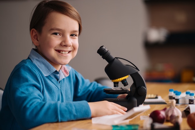 Junge der ersten Klasse, der zu Hause unter Verwendung des Mikroskops studiert