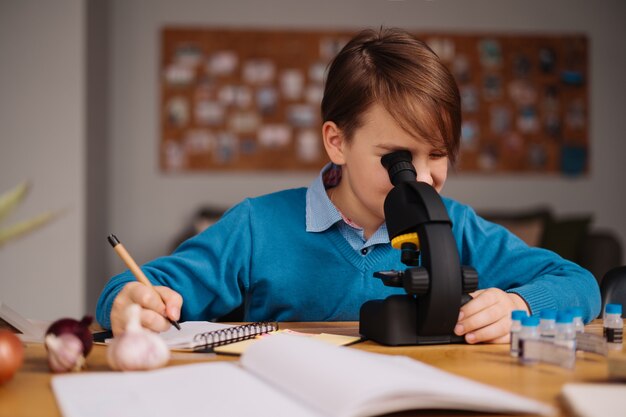 Junge der ersten Klasse, der zu Hause unter Verwendung des Mikroskops studiert