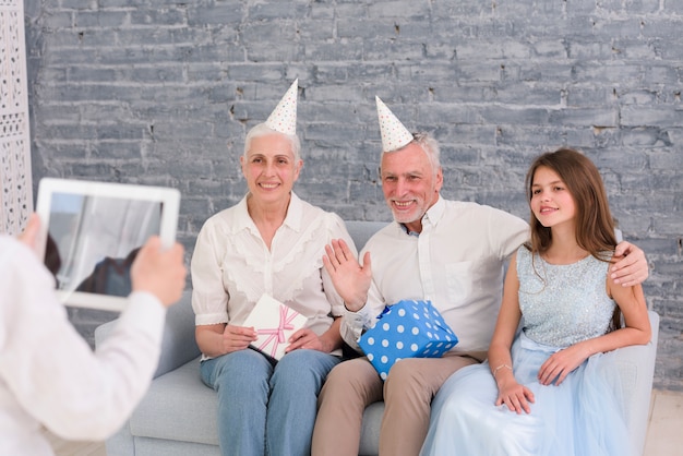 Junge, der Foto seiner Großeltern und Schwester sitzt auf Sofa mit digitaler Tablette macht