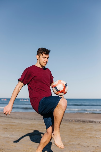 Kostenloses Foto junge, der fußball am strand spielt