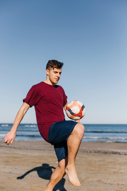 Junge, der Fußball am Strand spielt