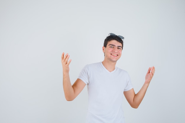 Junge, der Hände anhebt, während Kamera in T-Shirt betrachtet und fröhlich, Vorderansicht schaut.