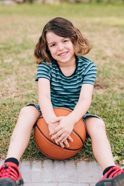 Kostenloses Foto junge, der im gras mit basketball sitzt