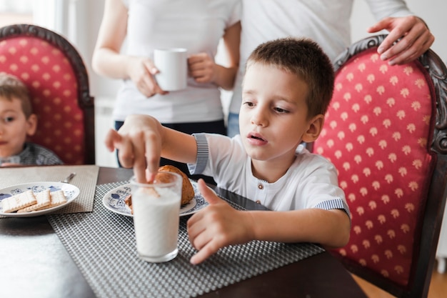 Junge, der Keks im Glas Milch eintaucht