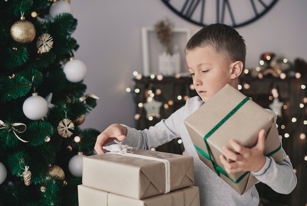 Junge, der neben Weihnachtsbaum steht und Geschenke nimmt