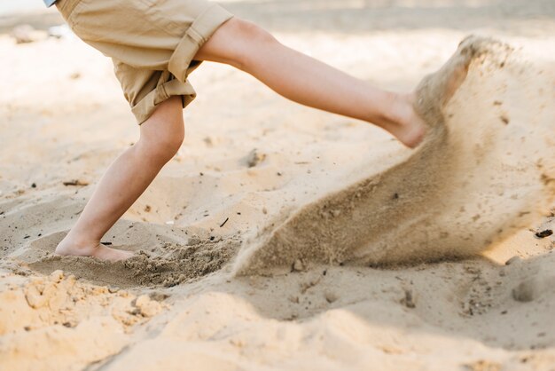 Junge, der Sand am Strand tritt