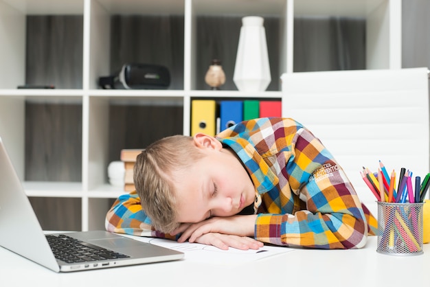 Junge, der vor Laptop auf Schreibtisch schläft