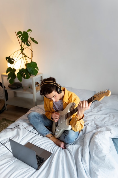 Kostenloses Foto junge, der zu hause gitarre spielt, hoher winkel