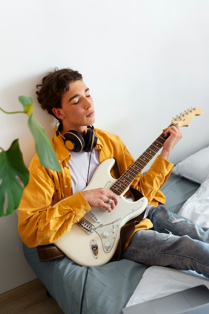 Kostenloses Foto junge, der zu hause gitarre spielt, hoher winkel