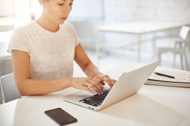 Junge Drehbuchautorin, die einen Laptop verwendet, um ihren ersten Bestseller-Roman zu erstellen, der optimistisch aussieht.