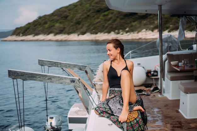 Junge dünne Frau, die im Bikinibadeanzug auf einer Yacht sitzt und in der Sonne sich aalt