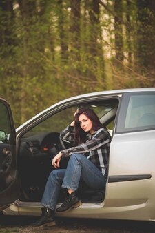 Junge dunkelhaarige kaukasische frau in einem karierten hemd posiert in einem auto