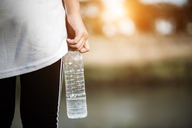 Junge Eignungsfrauenhand, die Wasserflasche hält, nachdem Übung laufen gelassen worden ist