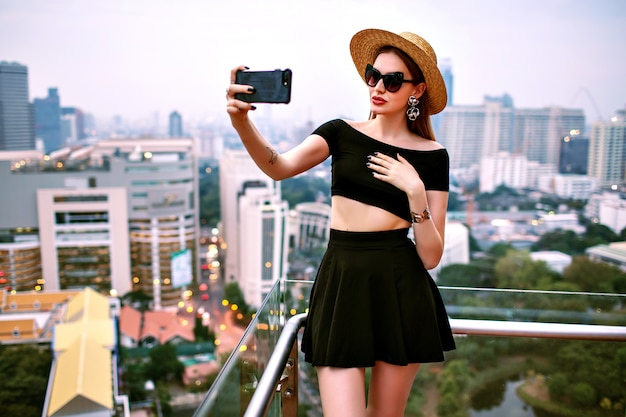 Junge elegante Frau, die modisches trendiges Sommeroutfit trägt, das touristisches Selfie an der Terrasse des Luxushotels macht