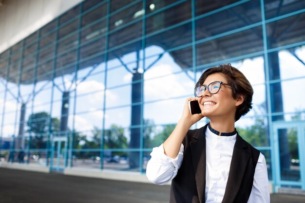 Junge erfolgreiche Geschäftsfrau, die am Telefon spricht und nahe Geschäftszentrum steht.