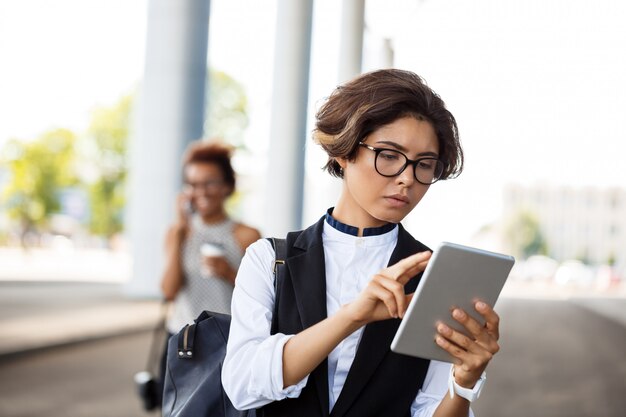 Junge erfolgreiche Geschäftsfrau, die Tablette über Geschäftszentrum betrachtet.