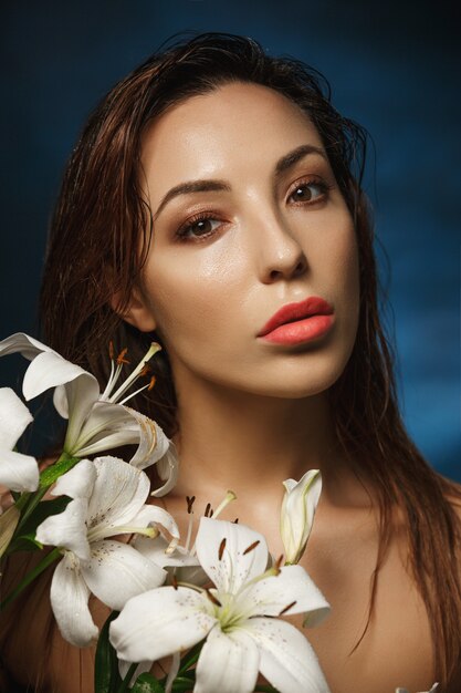 Junge erstaunliche Frau, die hemdlos hinter zarten Blumen steht. Modefotografie.