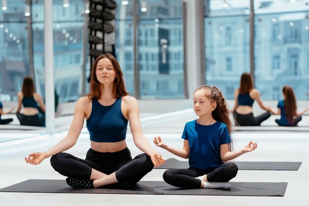 Junge erwachsene Mutter und kleine Tochter, die zusammen Yoga praktizieren
