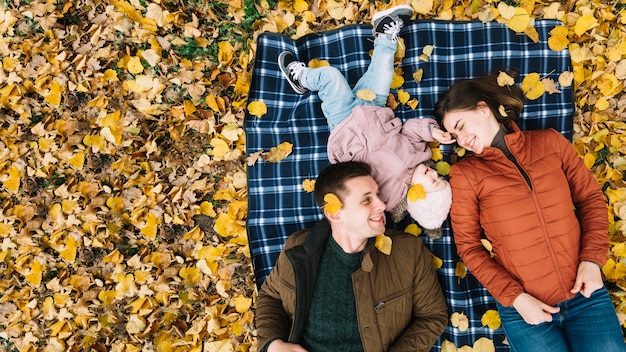 Kostenloses Foto junge familie, die auf herbstlaub im park liegt