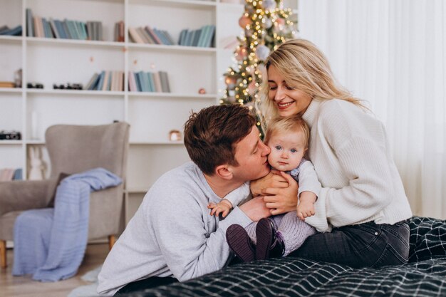 Junge Familie mit dem Baby, das durch Weihnachtsbaum sitzt