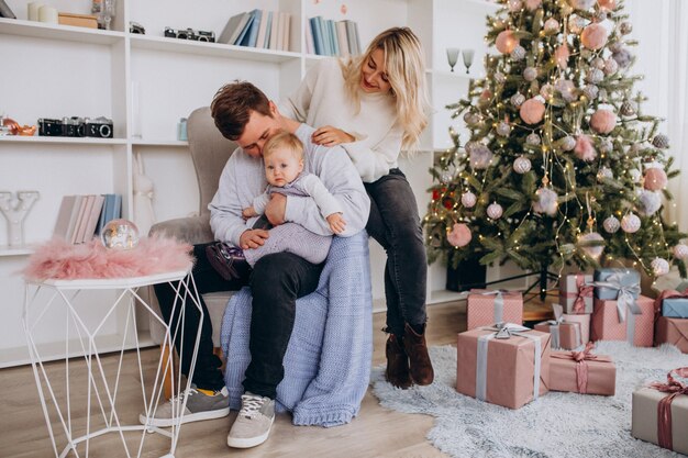 Junge Familie mit dem Baby, das durch Weihnachtsbaum sitzt