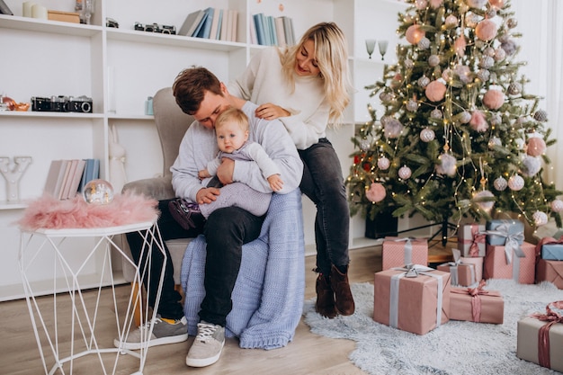 Junge Familie mit dem Baby, das durch Weihnachtsbaum sitzt