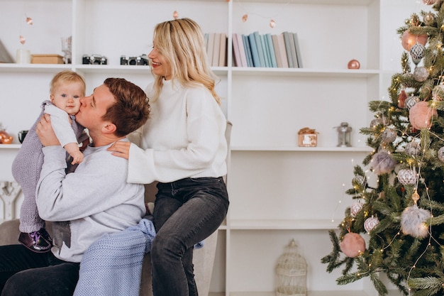 Junge Familie mit dem Baby, das durch Weihnachtsbaum sitzt