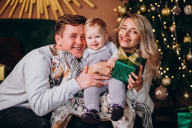 Junge Familie mit dem Baby, das durch Weihnachtsbaum sitzt