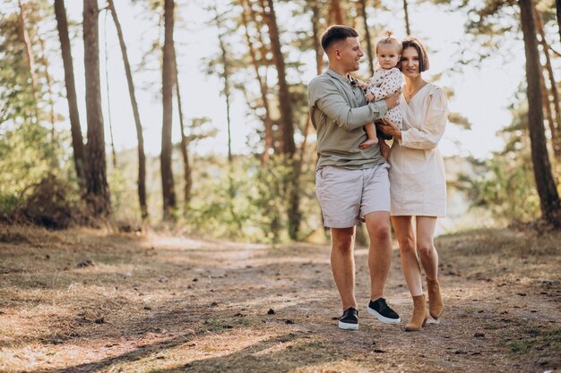 Junge Familie mit der niedlichen kleinen Tochter, die im Wald auf dem Sonnenuntergang geht