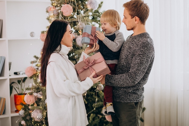 Junge Familie mit kleinem Sohn durch den Weihnachtsbaum, der Weihnachtsgeschenke hält