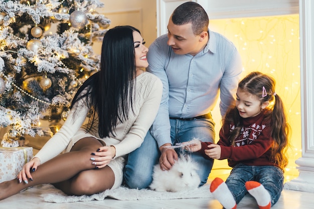 Junge Familie wirft vor einem glänzenden Weihnachtsbaum in einem gemütlichen Luxuszimmer auf