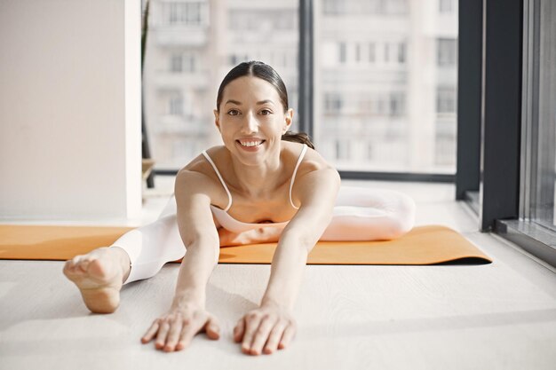 Junge Fitnessfrau, die Yoga macht und sich auf einer Matte im Studio mit großen Fenstern ausdehnt