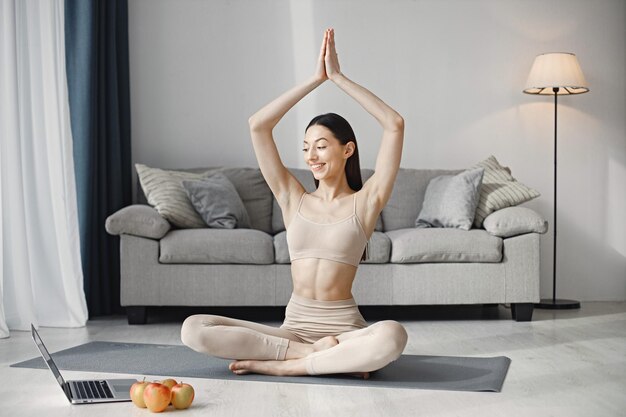 Junge Fitnessfrau, die zu Hause auf einer Yogamatte sitzt und einen Laptop benutzt