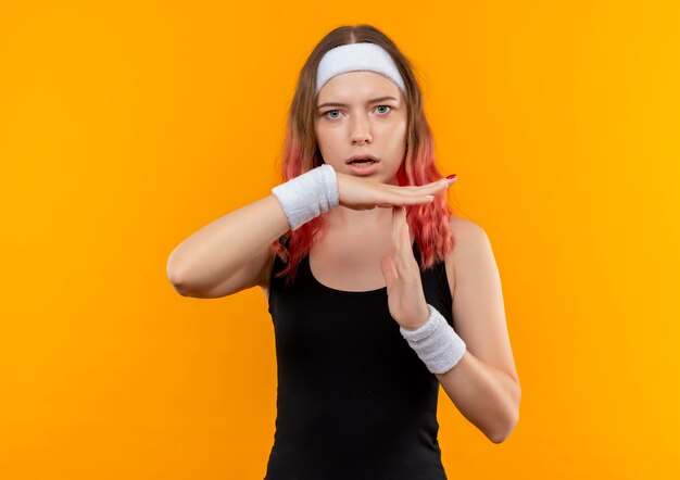 Junge Fitnessfrau in der Sportbekleidung verwirrte Auszeitgeste mit den Händen, die über orange Wand stehen