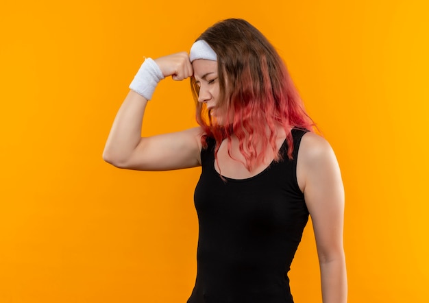 Junge Fitnessfrau in Sportbekleidung, die verwirrten berührenden Kopf für Fehler sucht