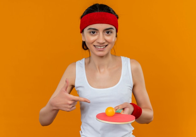 Junge Fitnessfrau in Sportbekleidung mit Stirnband, das Schläger und Ball für Tischtennis hält