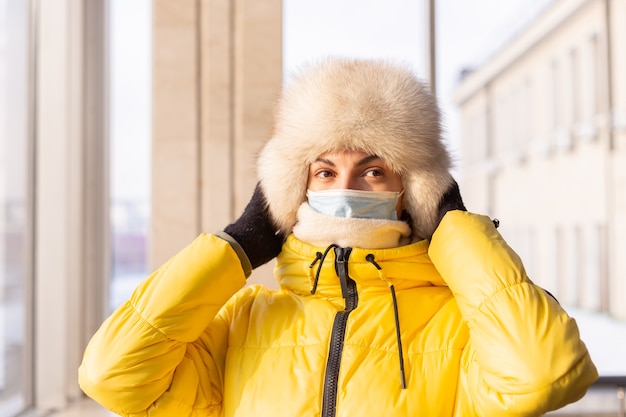 Junge Frau am Bahnhof in einer Schutzmaske auf dem Gesicht im Winterkleidungspassagier