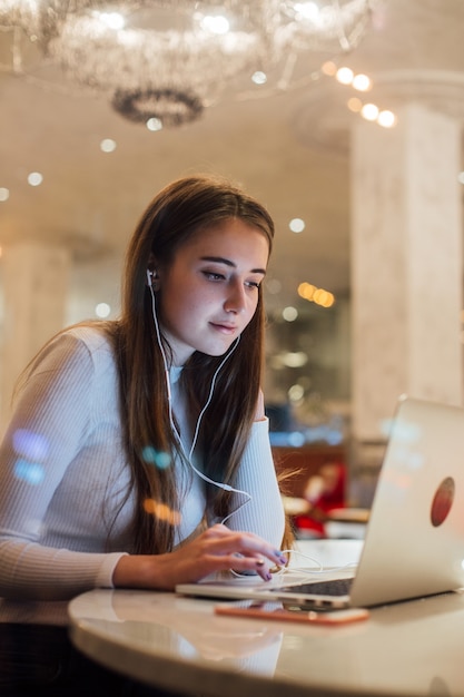 Junge Frau arbeitet am Laptop in den Kopfhörern im Büro