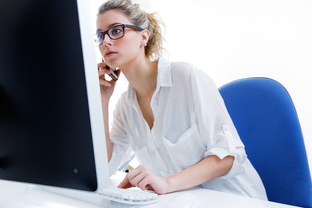 Junge Frau arbeitet von zu Hause auf dem Computer und reden am Telefon mit dem Büro