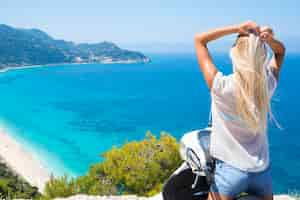 Kostenloses Foto junge frau auf dem motorrad durch das meer, das die ansicht am strand genießt